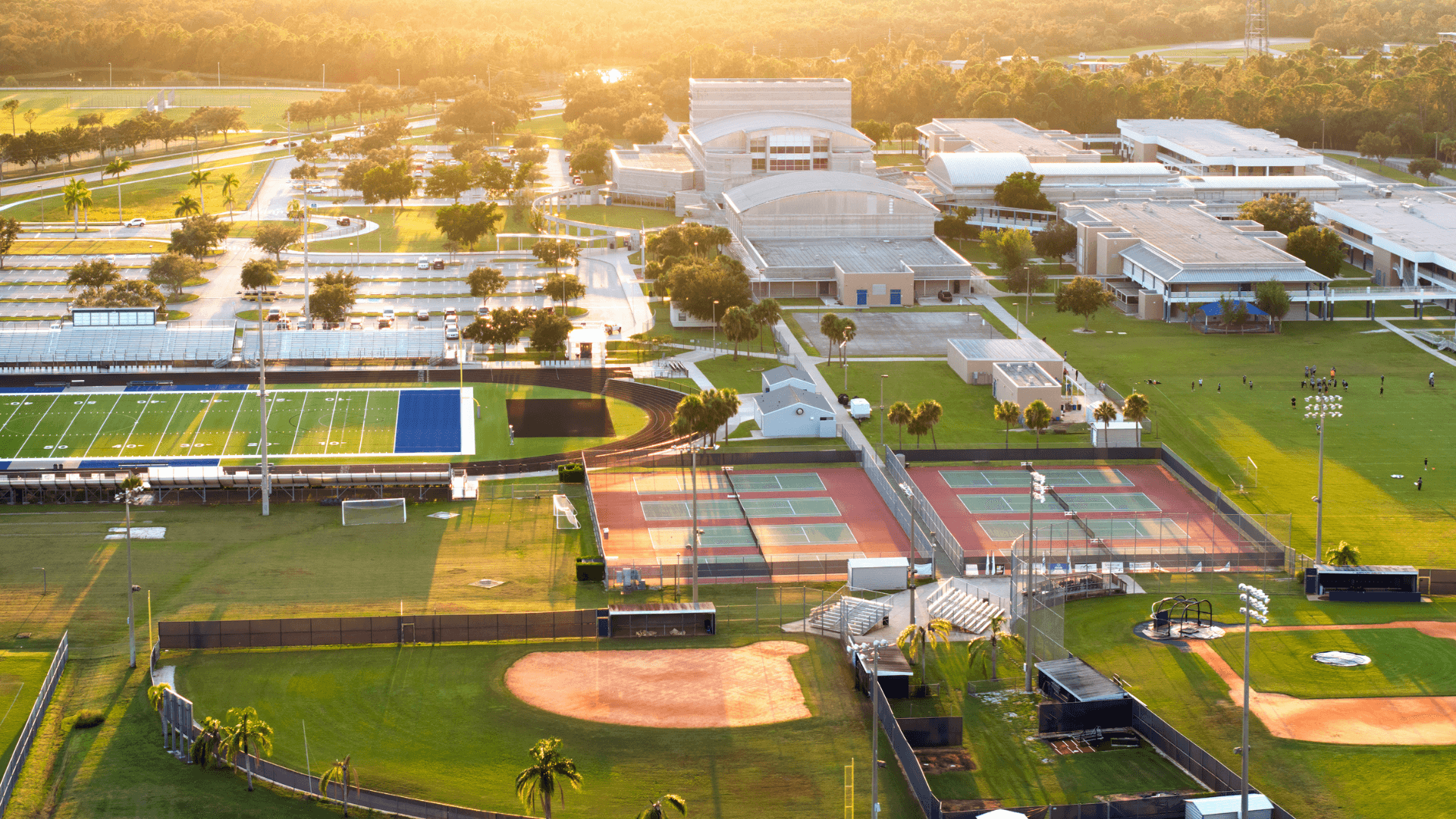arial shot of a sports complex with a football field with a track around it, tennis courts, two baseball diamonds, a soccer pitch, various buildings, and a parking lot